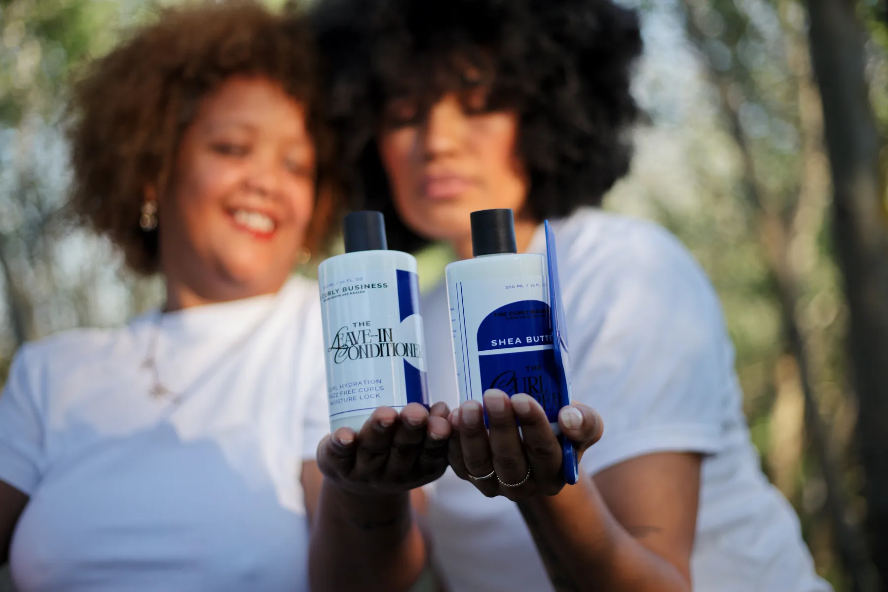 Women holding The Curly Business hair care products